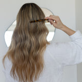 Person combing long, wavy hair with a VESITIA comb in a neutral setting
