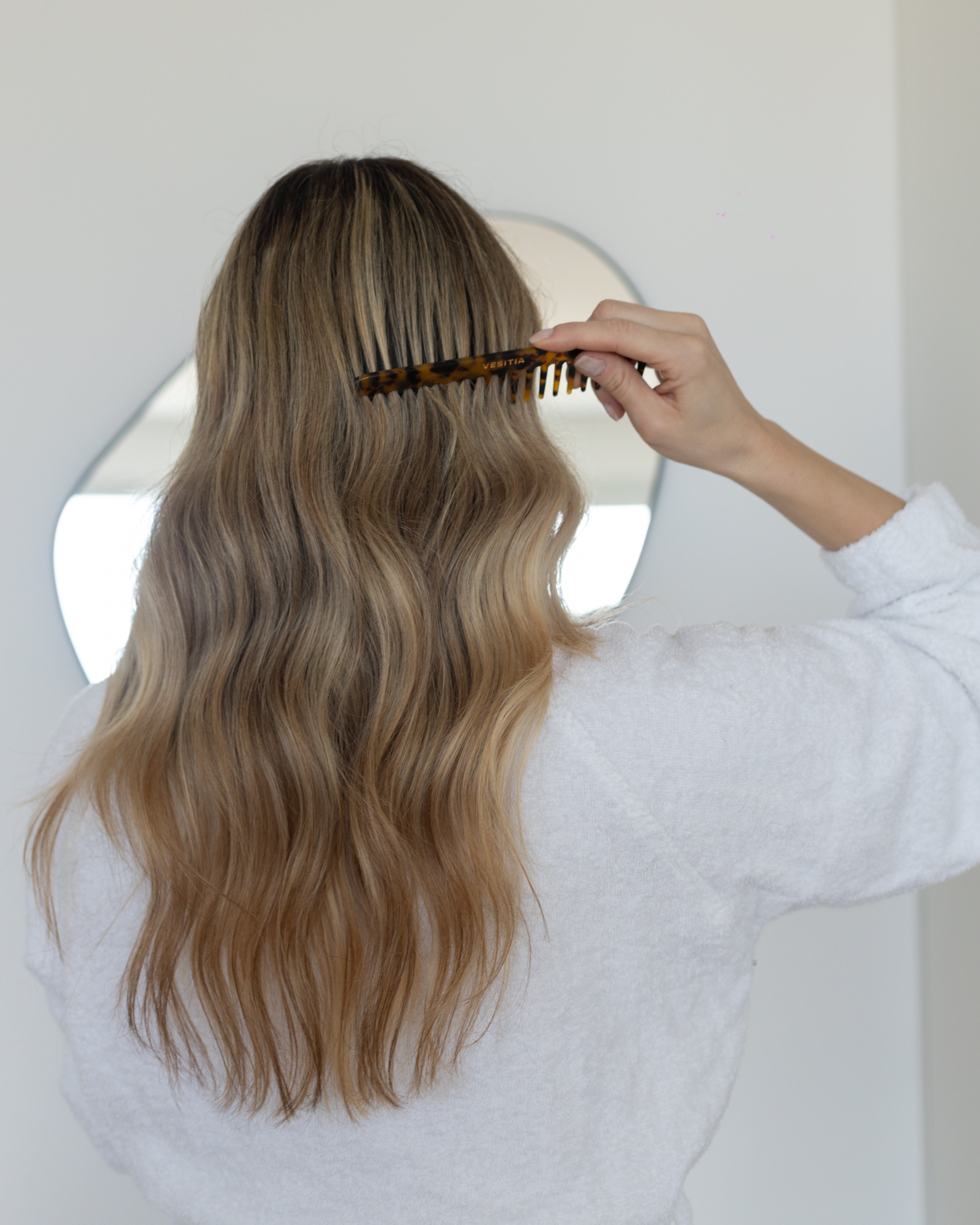 Person combing long, wavy hair with a VESITIA comb in a neutral setting