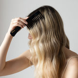 Person with long blonde hair using a black VESITIA comb on a plain background