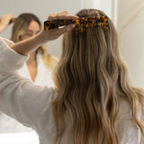 Person styling her hair with a VESITIA comb in a bathroom setting.