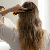 Person styling long blonde hair with a VESITIA comb in a bright room.