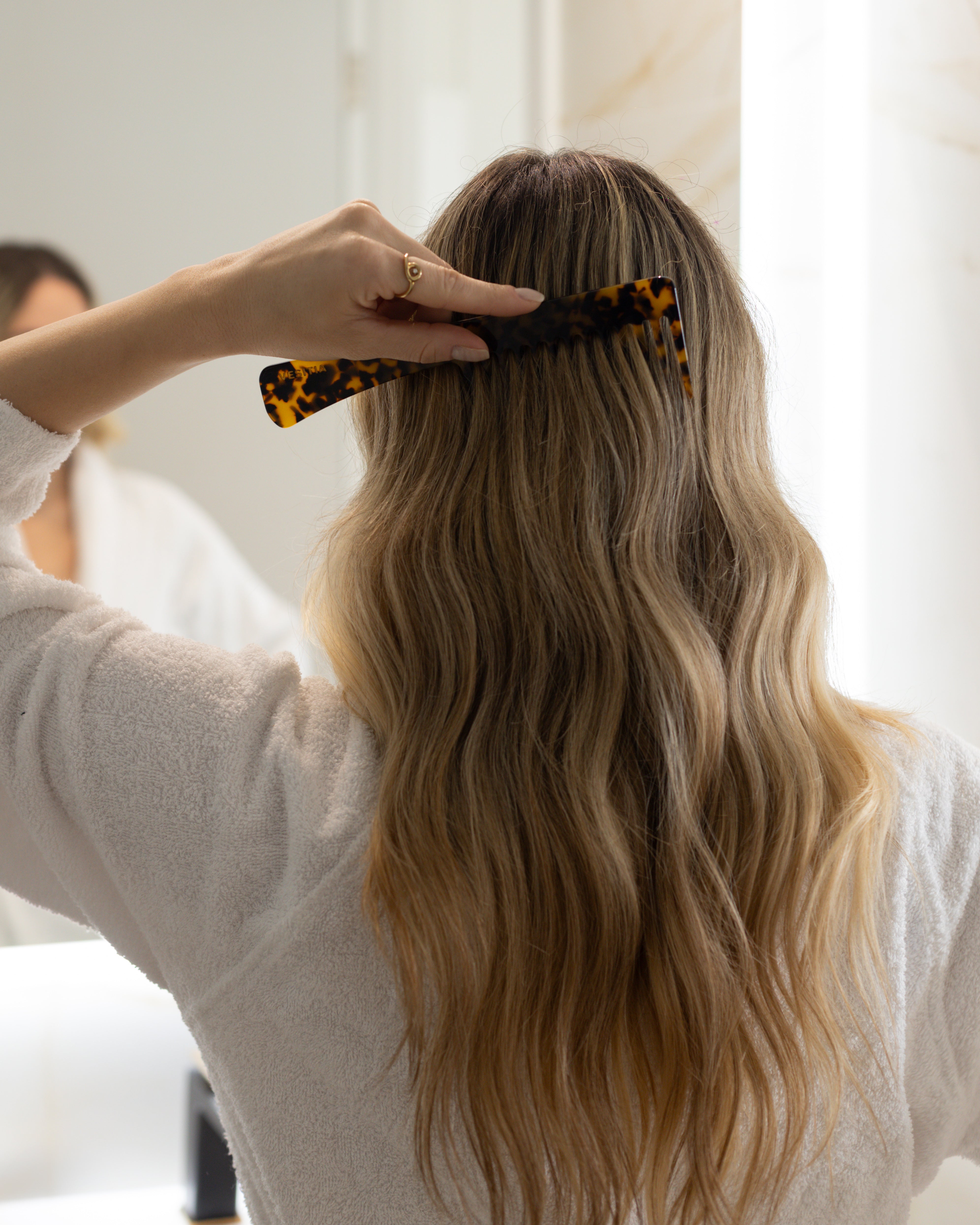 Person styling long blonde hair with a VESITIA comb in a bright room.