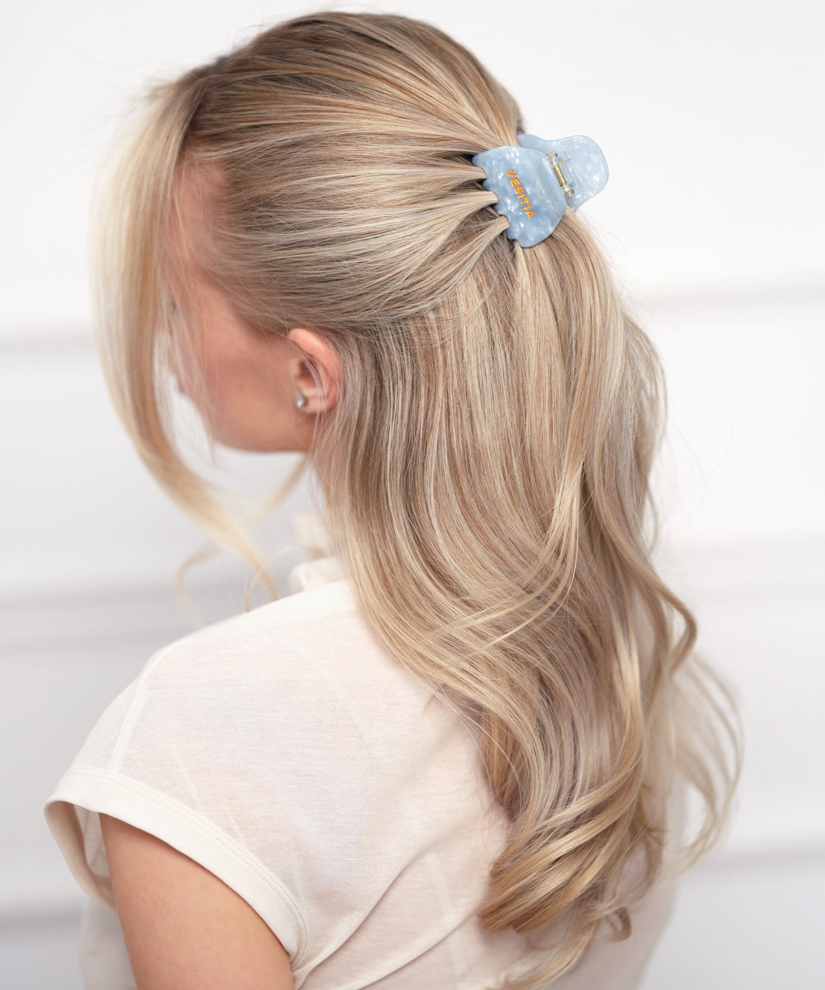 Woman with blonde hair wearing a blue VESITIA claw clip on a white background
