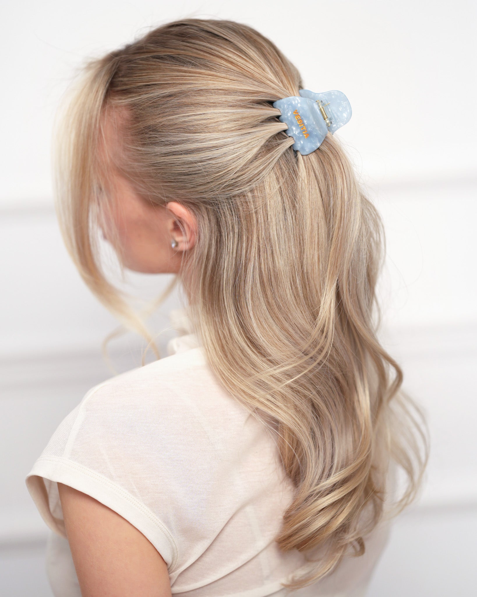 Woman with blonde hair wearing a blue VESITIA claw clip on a white background