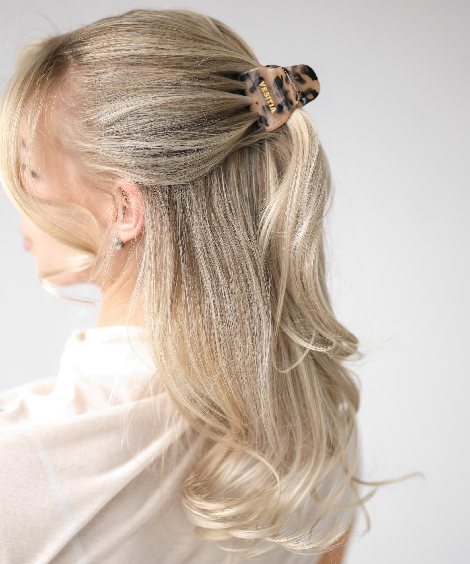 Blonde hair styled in a half up half down style with a VESITIA midi claw clip on a white background