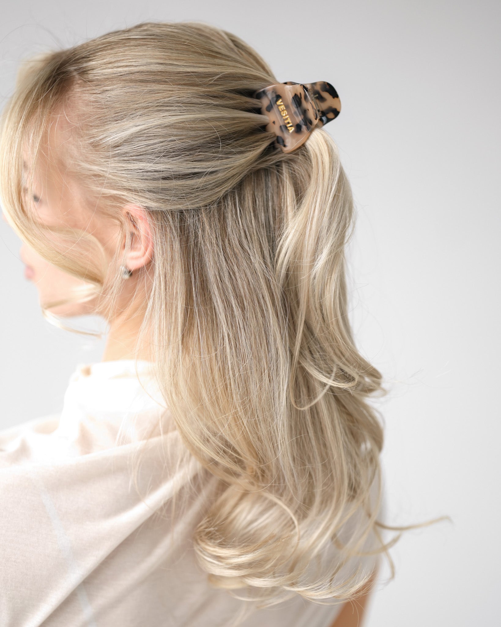 Blonde hair styled in a half up half down style with a VESITIA midi claw clip on a white background