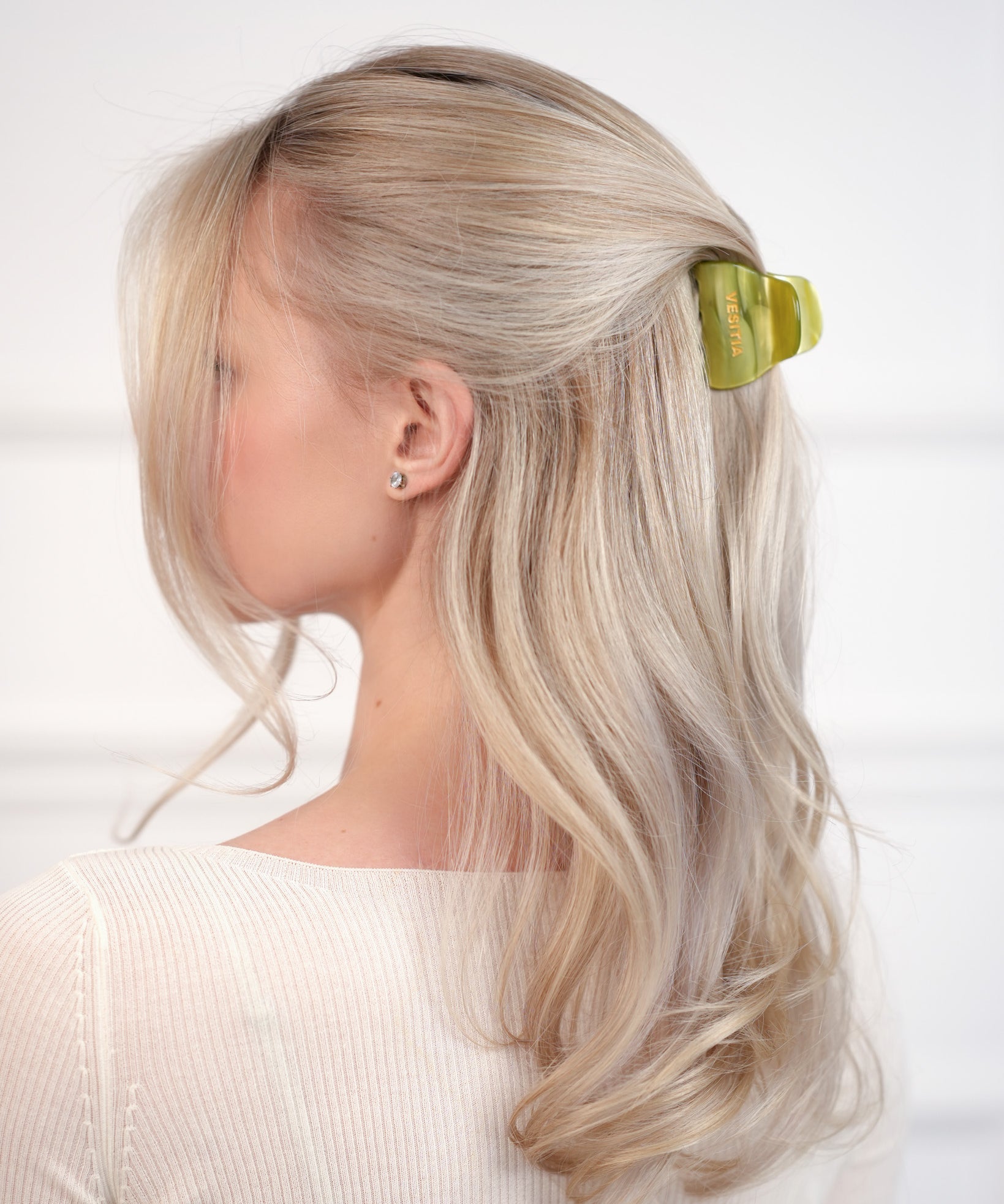 Woman with blonde hair wearing a green VESITIA claw clip against a white background