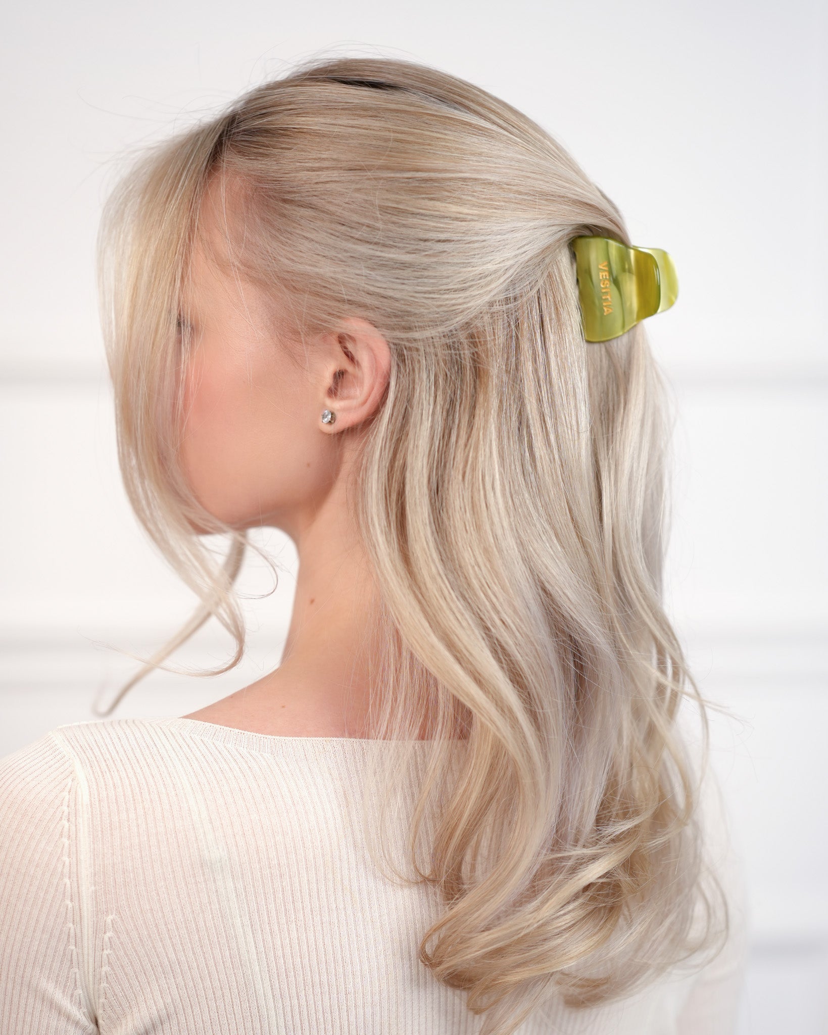 Woman with blonde hair wearing a green VESITIA claw clip against a white background