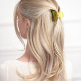 Blonde hair styled with a green VESITIA claw clip on a white background