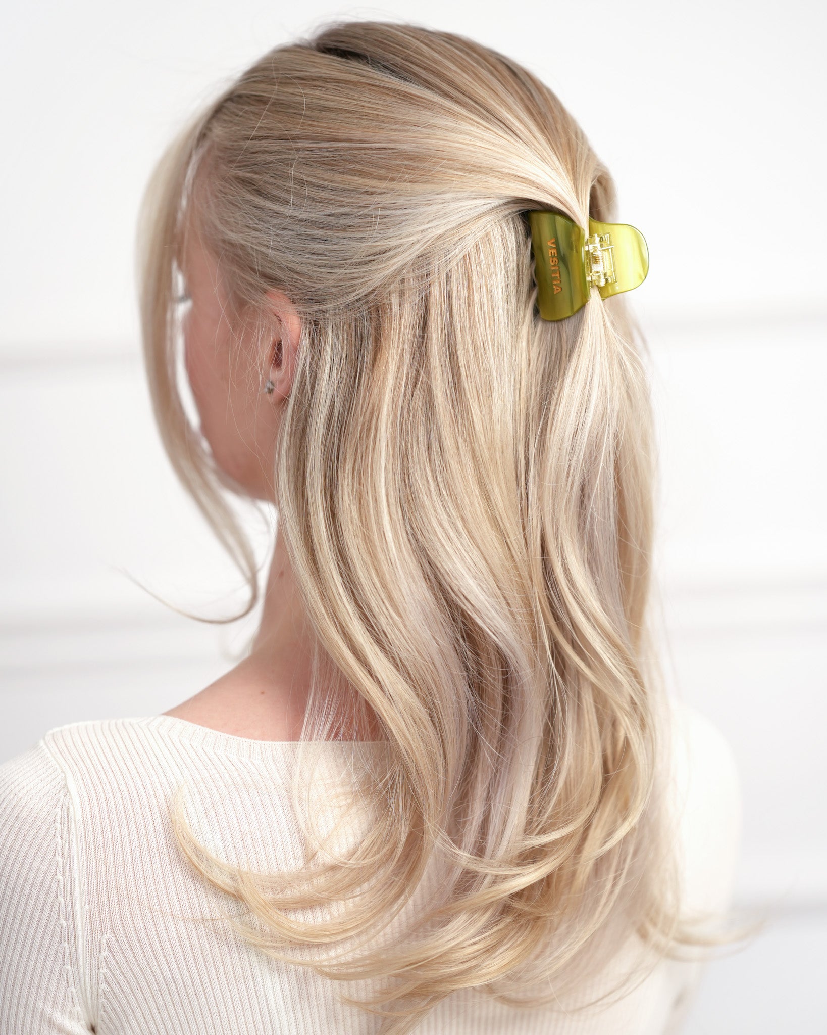 Blonde hair styled with a green VESITIA claw clip on a white background