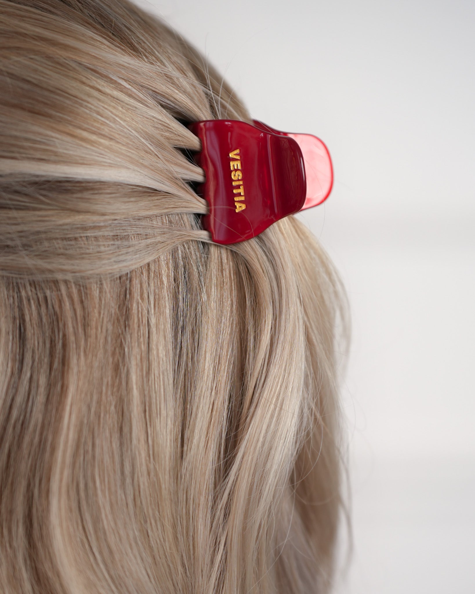 Red hair clip with 'VESITIA' branding on blonde hair against a white background