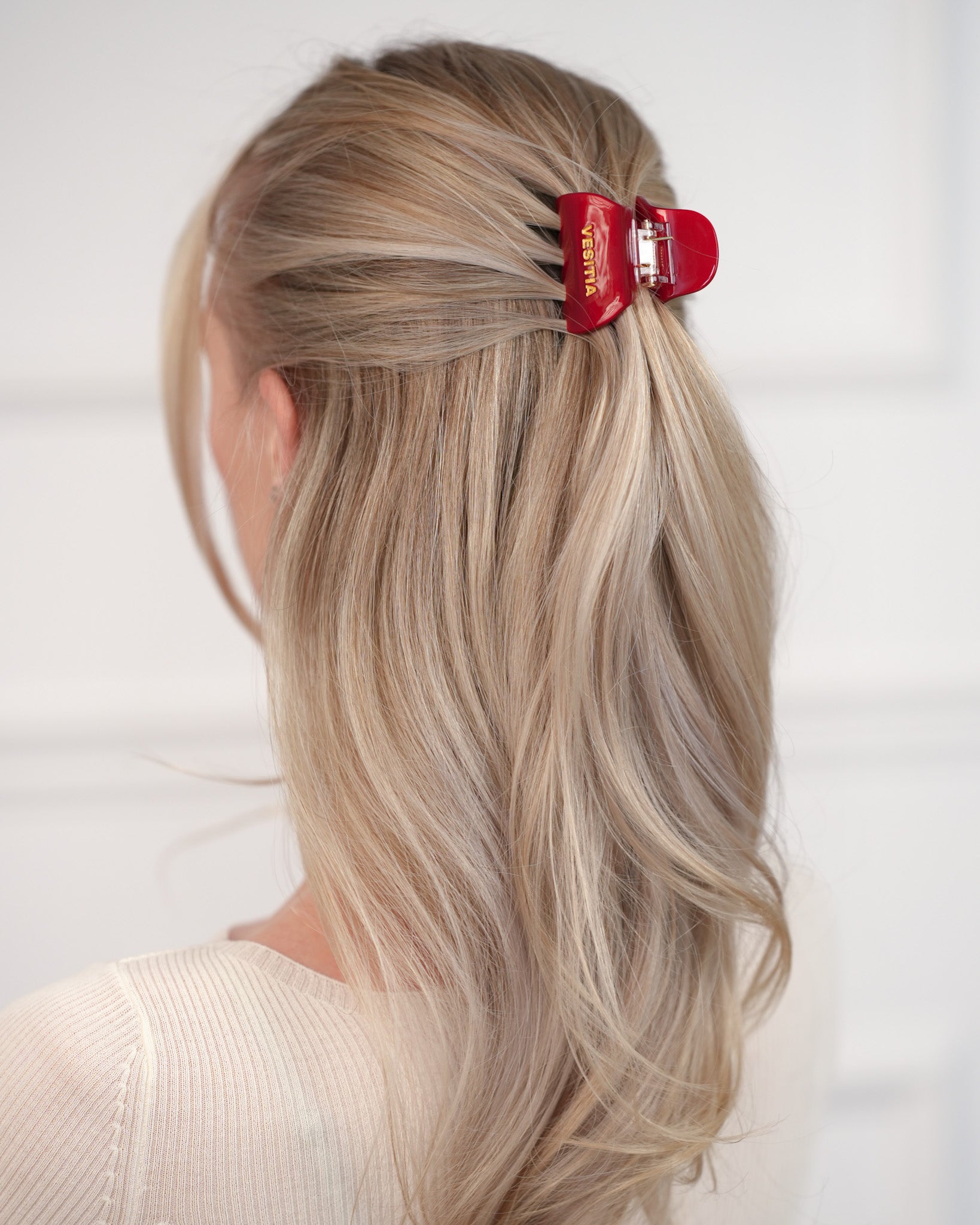 Blonde hair with a red VESITIA hair claw clip on a white background