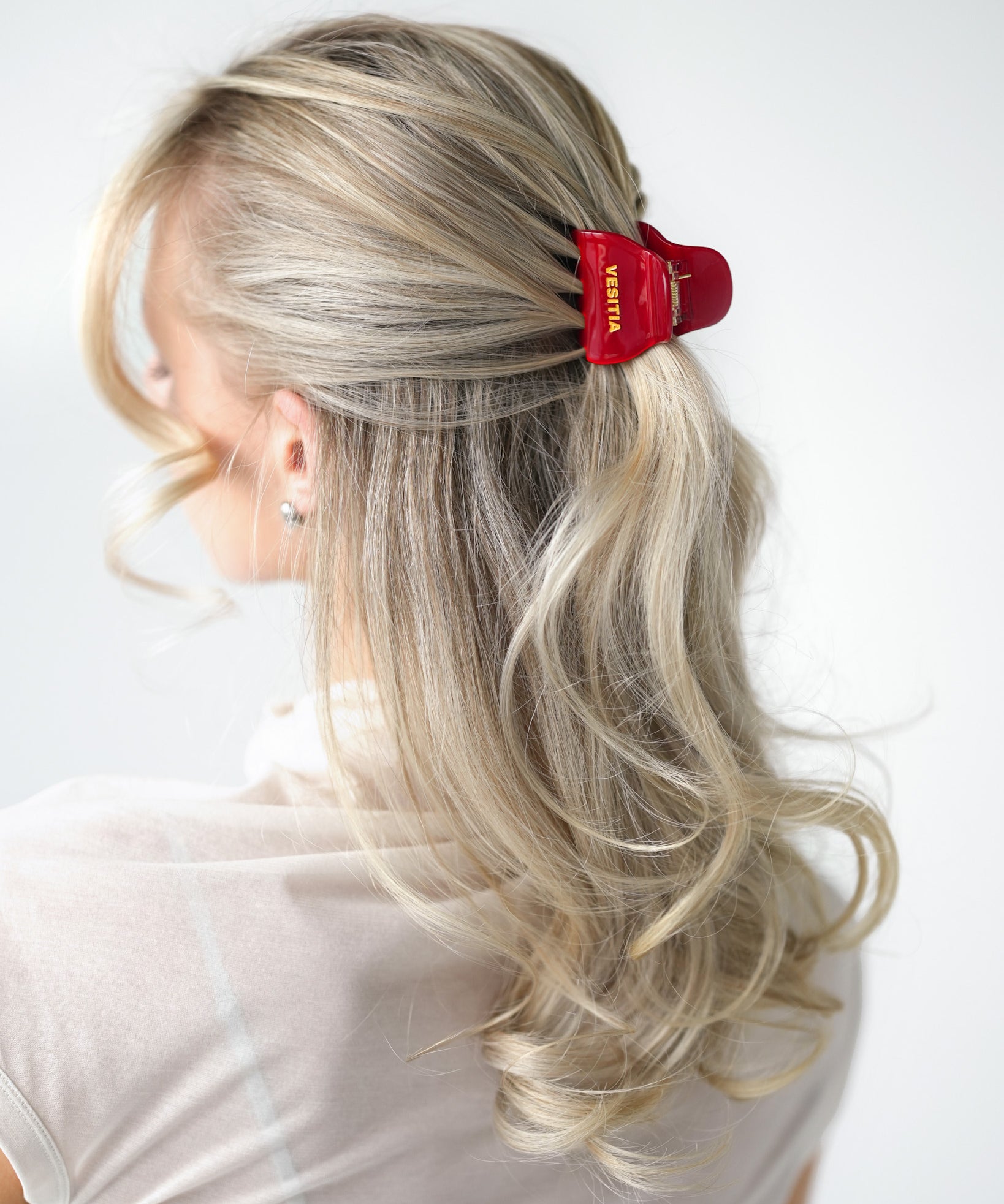 Person with blonde hair styled in half up half down style with a red VESITIA midi claw clip on a white background