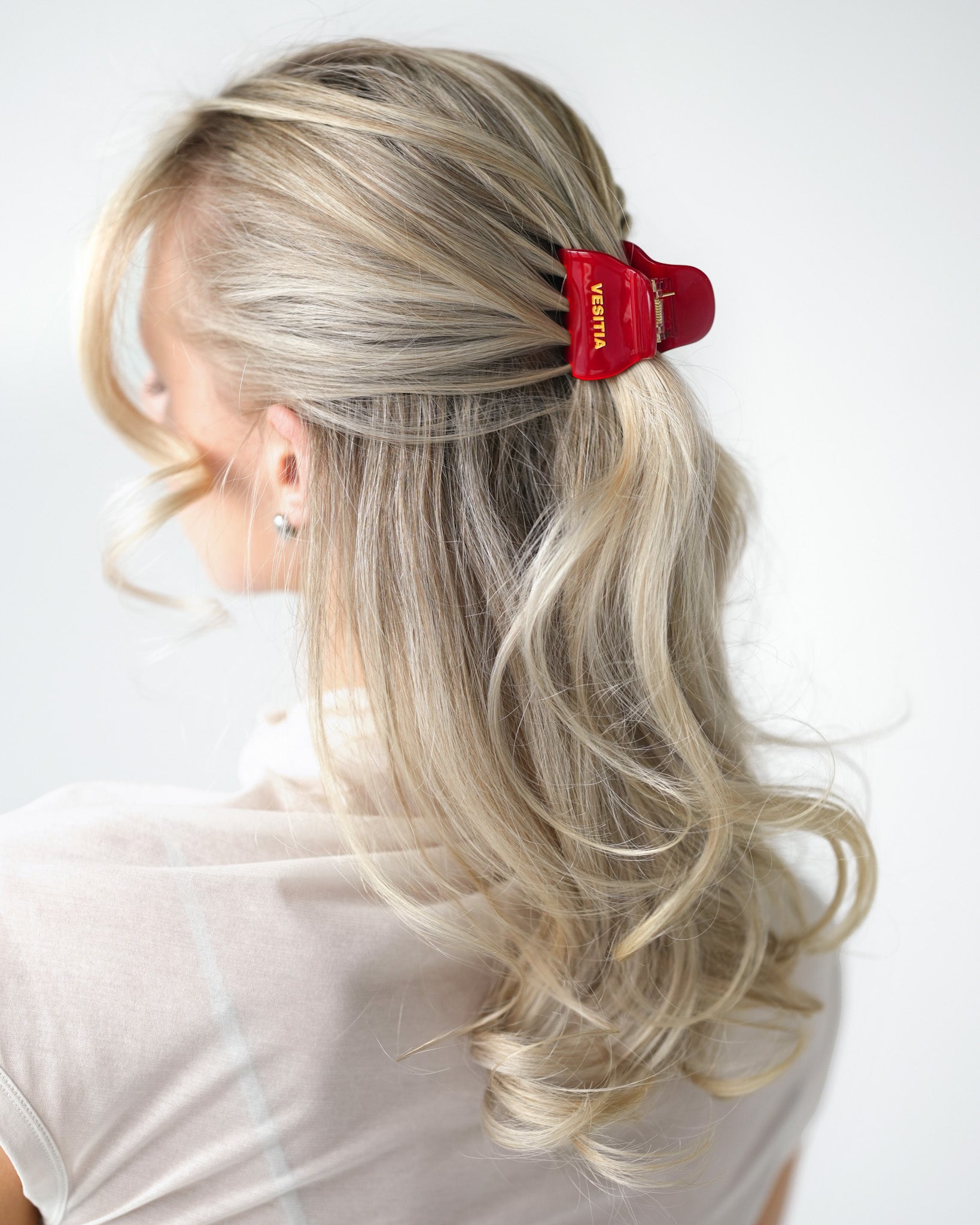 Person with blonde hair styled in half up half down style with a red VESITIA midi claw clip on a white background