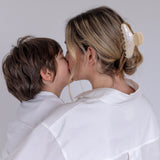 Woman in a white outfit wearing a VESITIA mother claw clip kissing a child on a plain background