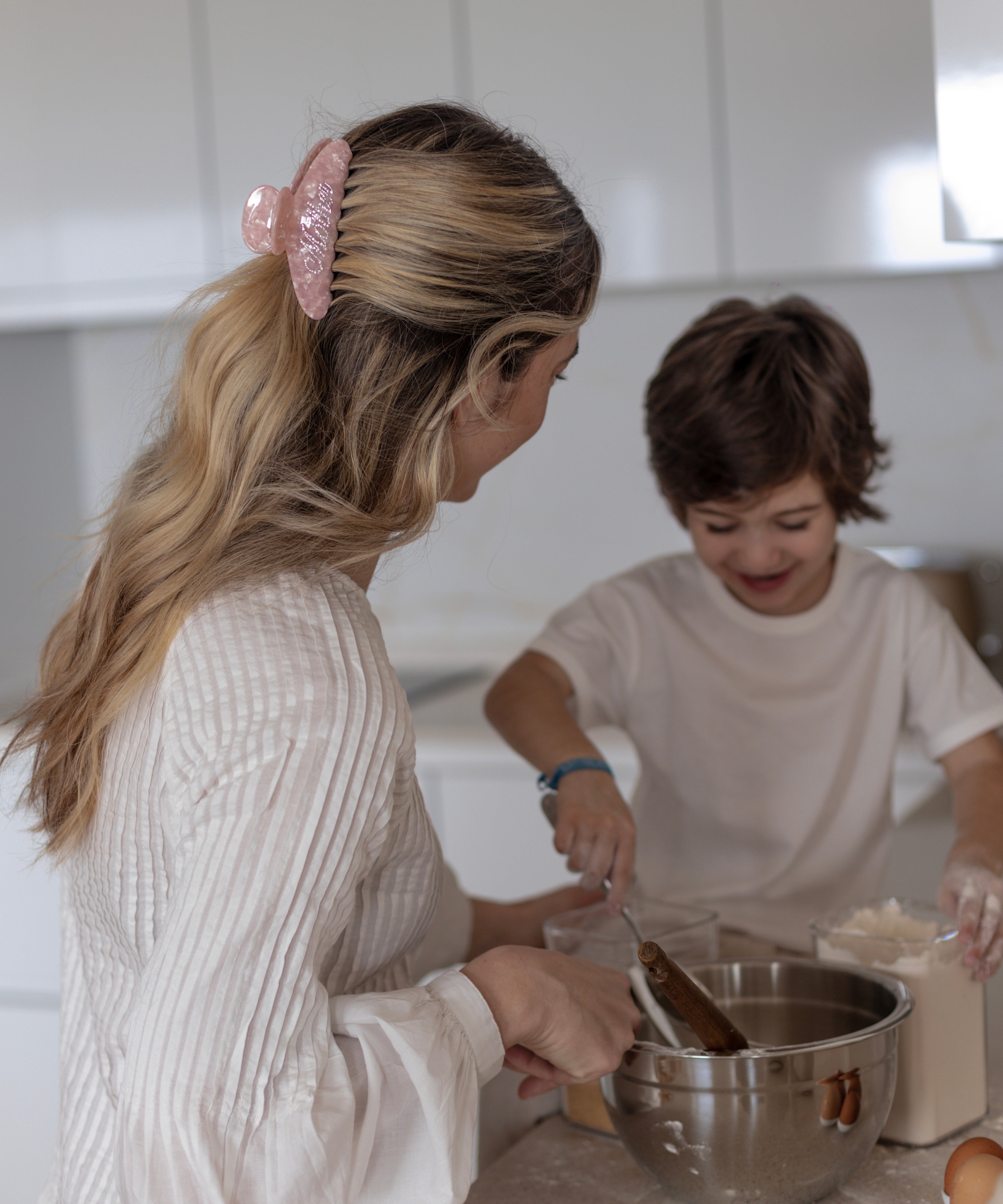 Woman wearing a pink VESITIA mother claw clip and child in a kitchen mixing ingredients in a bowl.
