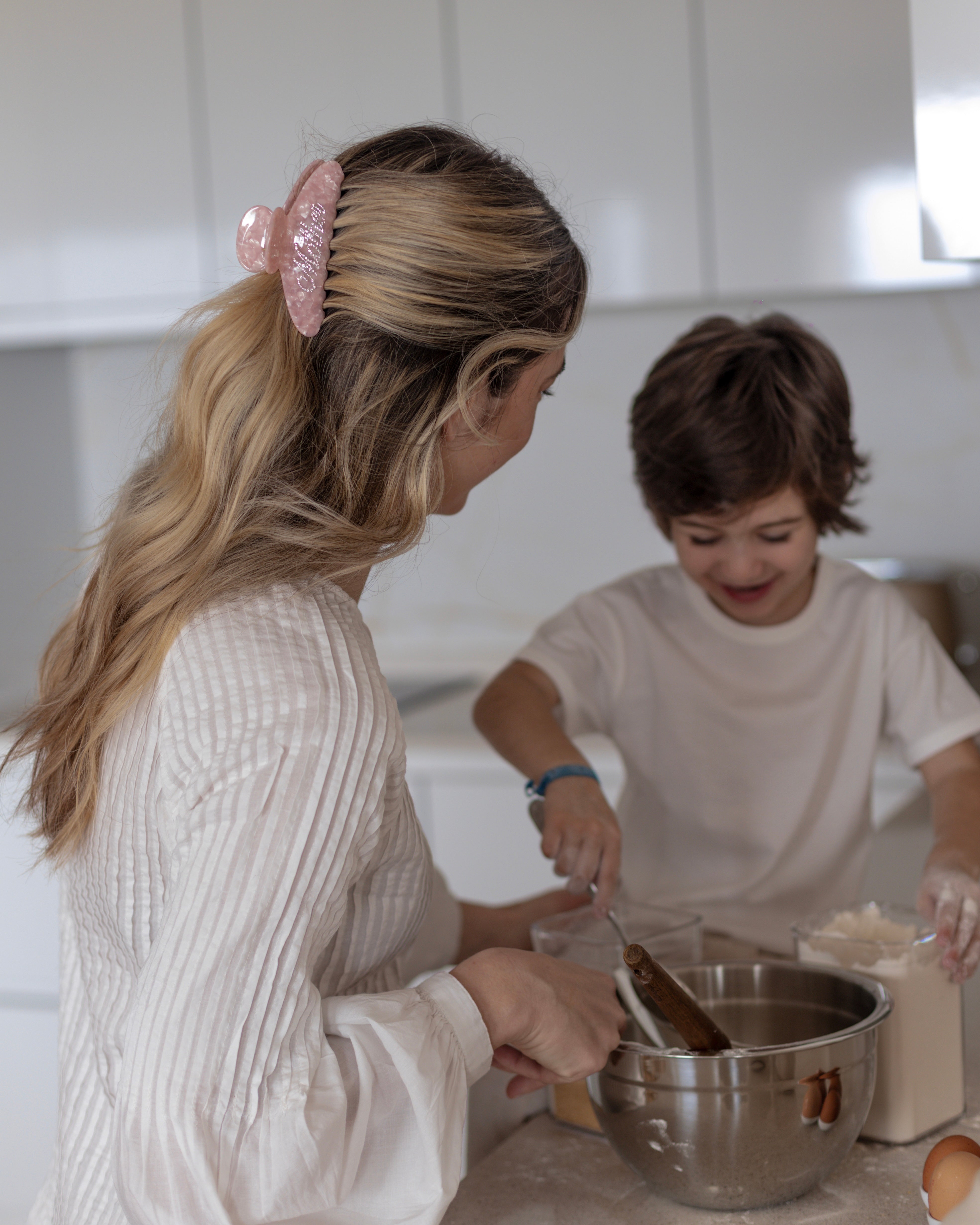 Woman wearing a pink VESITIA mother claw clip and child in a kitchen mixing ingredients in a bowl.