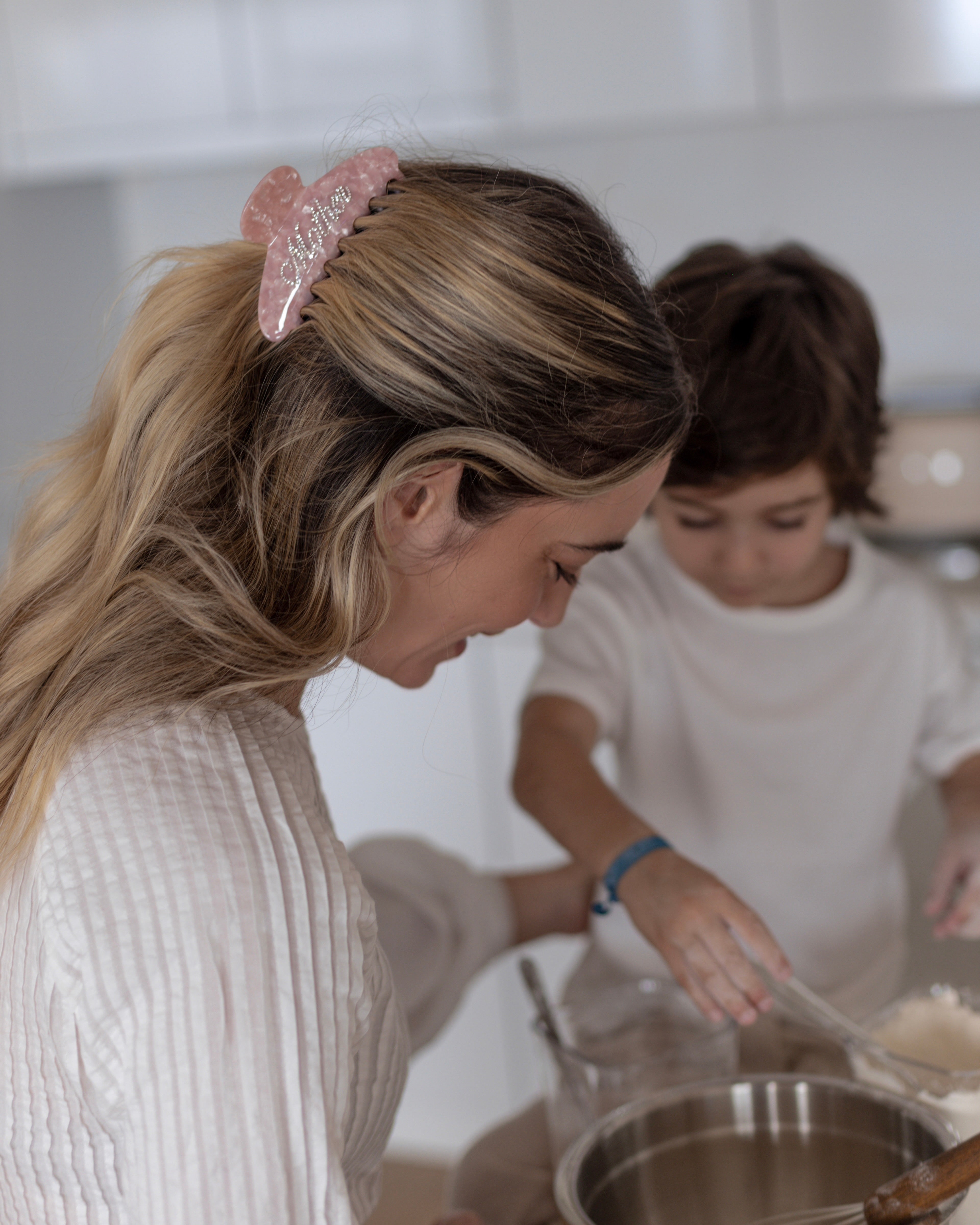Woman wearing a pink VESITIA mother claw clip and child in a kitchen preparing food together.