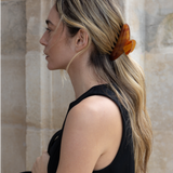 Woman wearing an orange VESITIA hair claw clip against a stone wall background