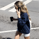 Woman walking on a street, hair styled with a VESITIA claw clip, talking on a phone and holding a coffee cup.