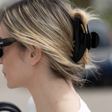 Person with blonde hair tied back with a black VESITIA claw clip, wearing sunglasses.