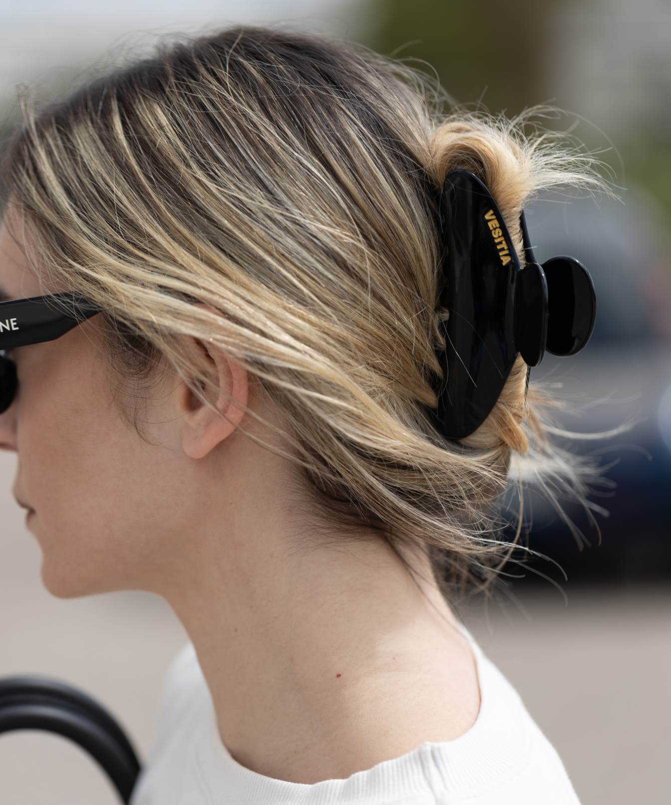 Person with blonde hair tied back with a black VESITIA claw clip, wearing sunglasses.