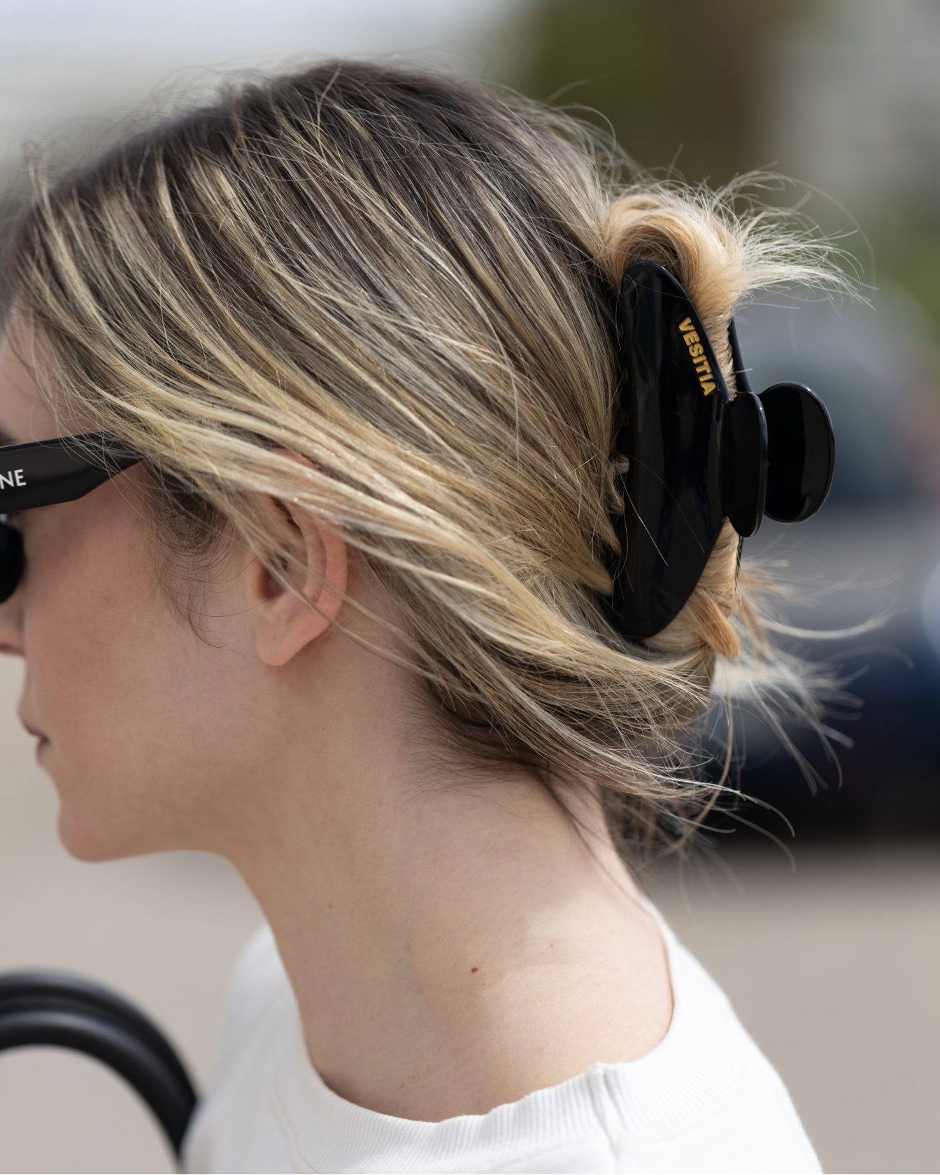 Person with blonde hair tied back with a black VESITIA claw clip, wearing sunglasses.