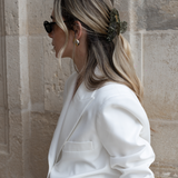 Woman with blonde hair wearing a VESITIA claw clip and a white blazer against a stone wall.