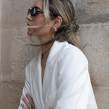 Woman in a white outfit with a VESITIA claw clip, sunglasses and a stone wall background