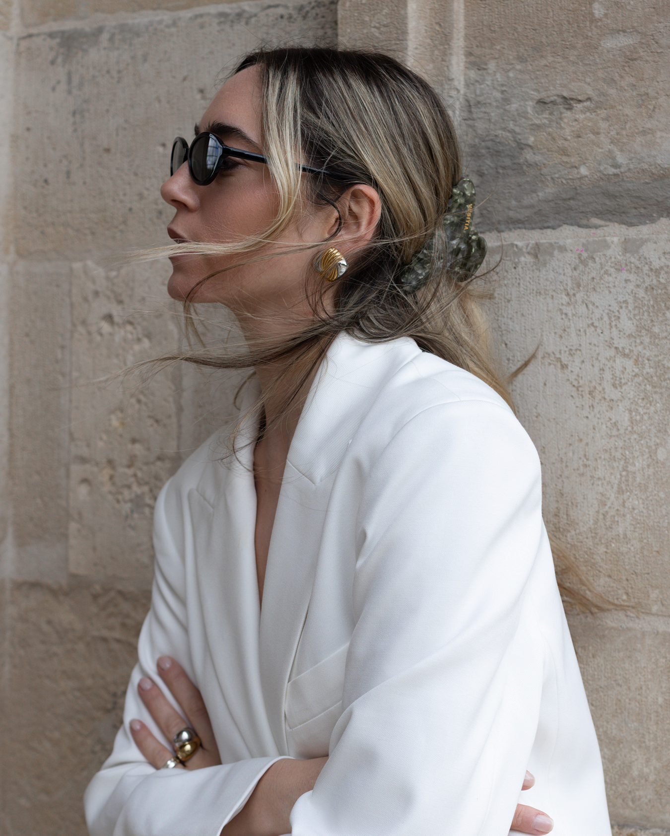 Woman in a white outfit with a VESITIA claw clip, sunglasses and a stone wall background