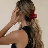 Woman with a red VESITIA claw clip in her blonde hair against a beige background