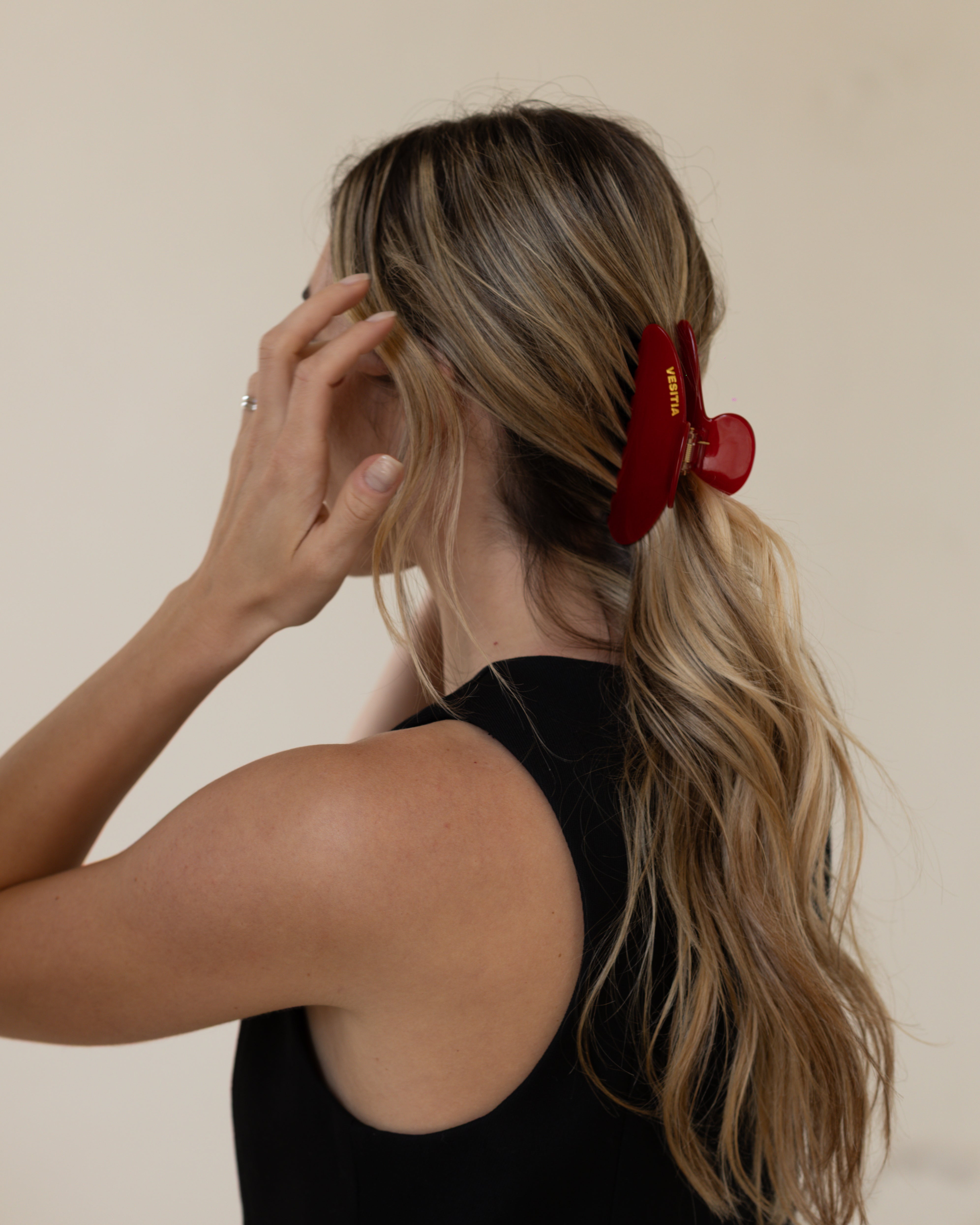 Woman with a red VESITIA claw clip in her blonde hair against a beige background
