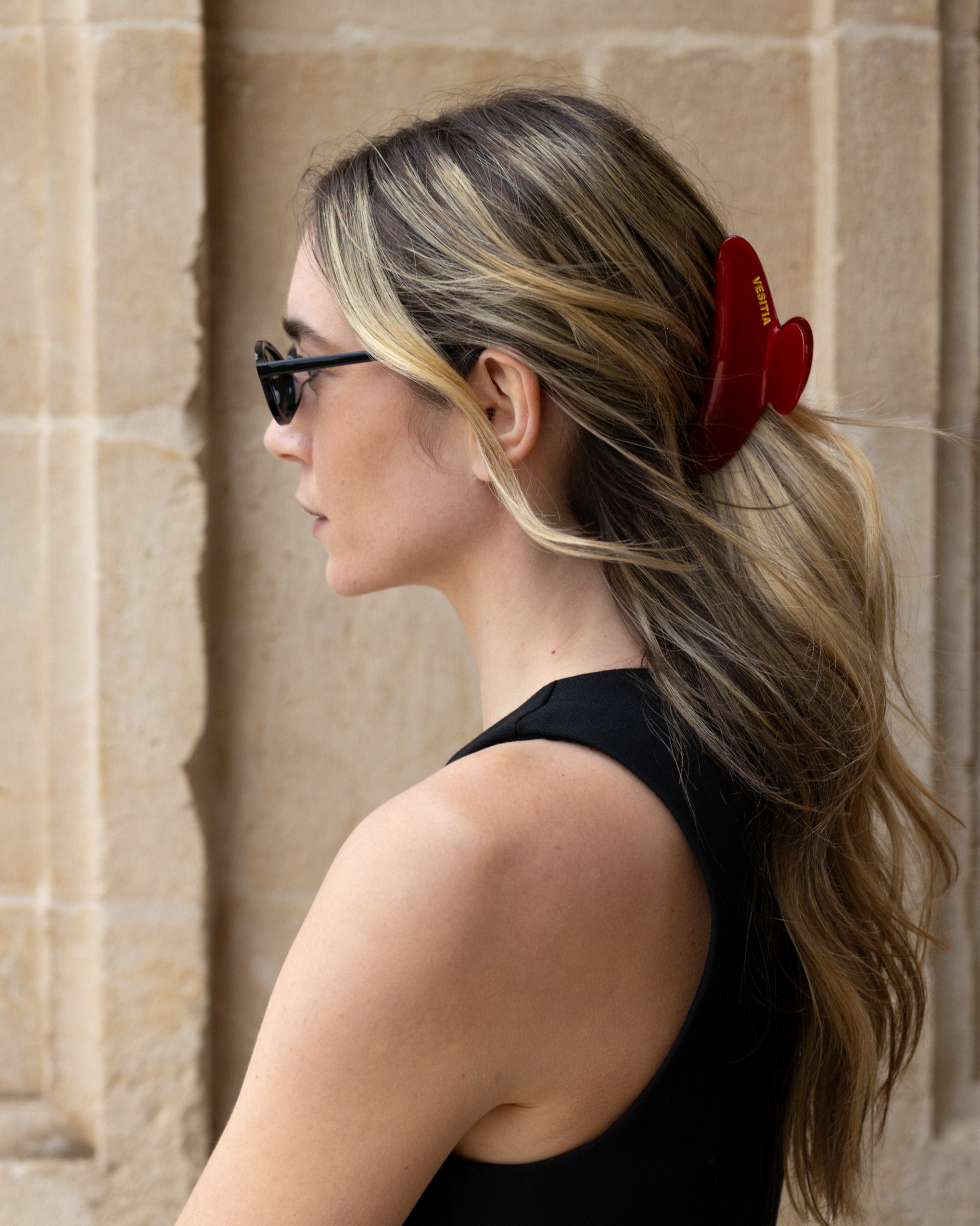 Woman with a red VESITIA hair claw clip in her hair against a stone wall background