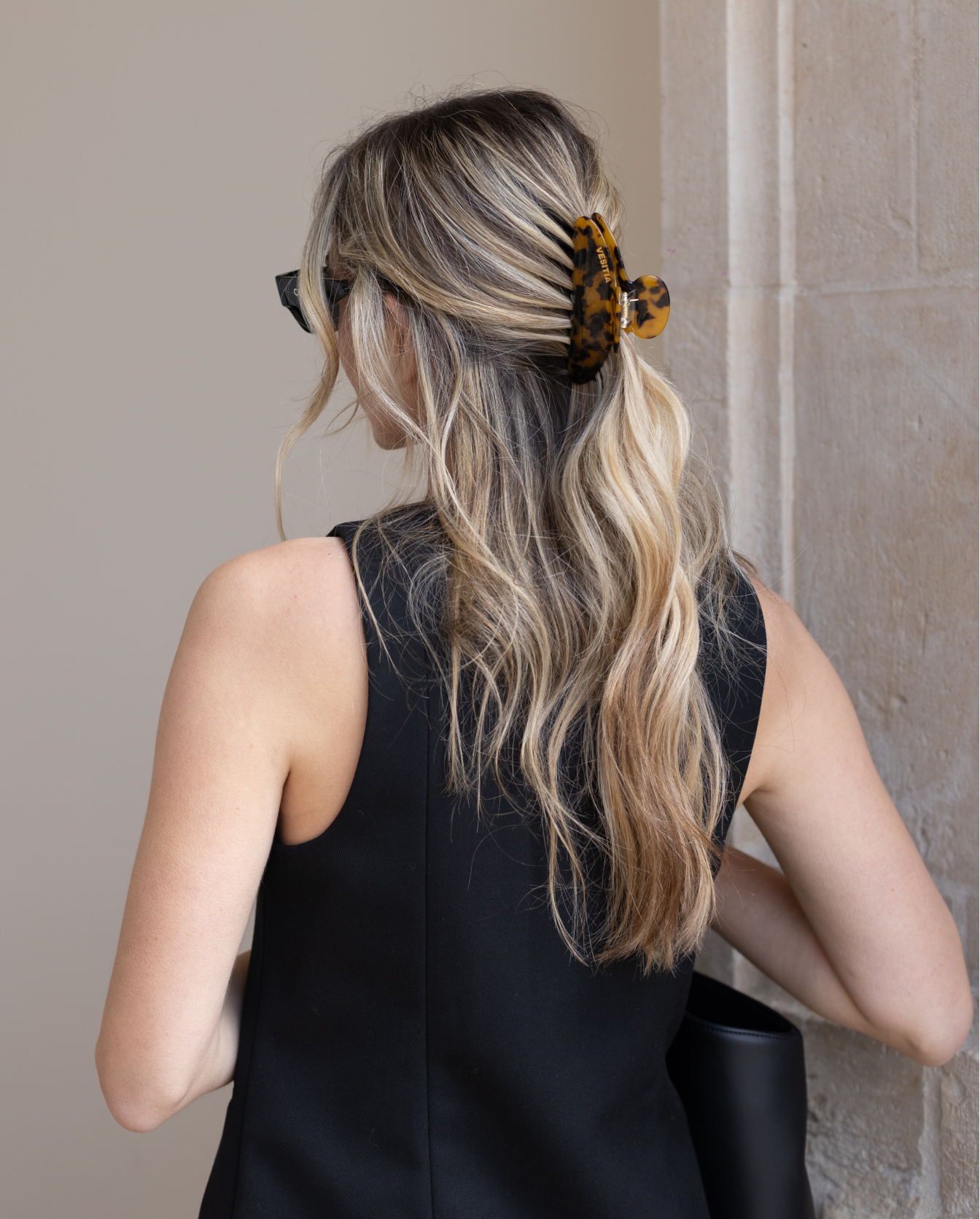 Woman with styled hair wearing a tortoise VESITIA claw clip and a black sleeveless top against a neutral wall.