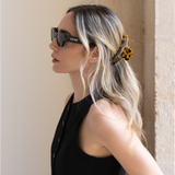Woman wearing sunglasses with a tortoise VESITIA claw clip against a neutral wall.