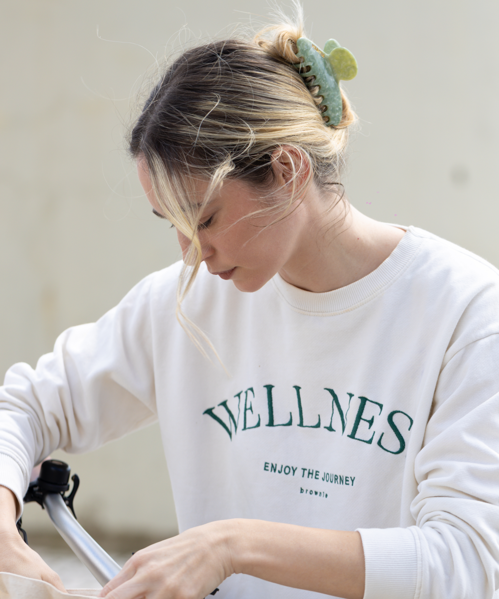Person wearing a white sweatshirt and a green VESITIA claw clip in her hair, holding a bag.