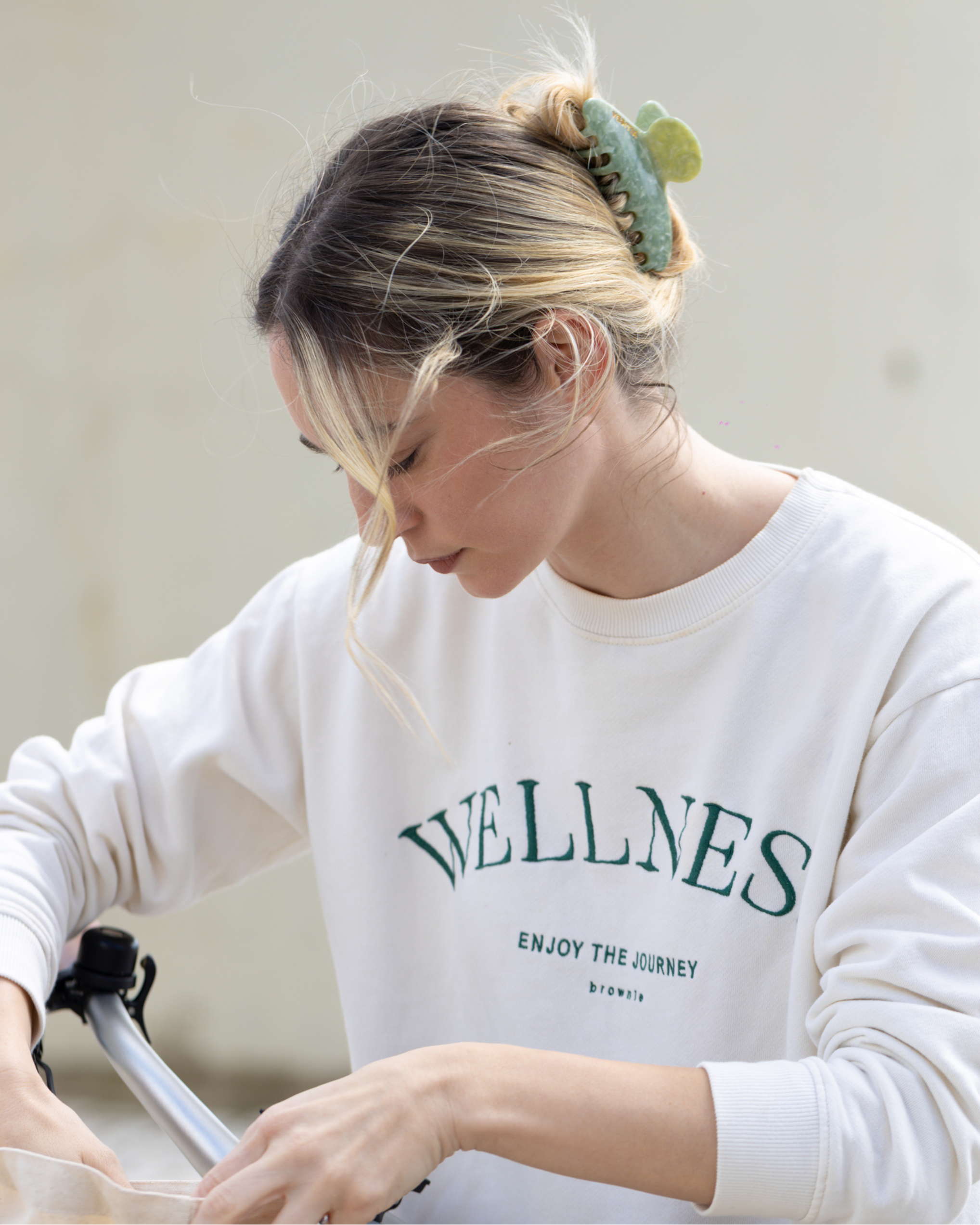 Person wearing a white sweatshirt and a green VESITIA claw clip in her hair, holding a bag.